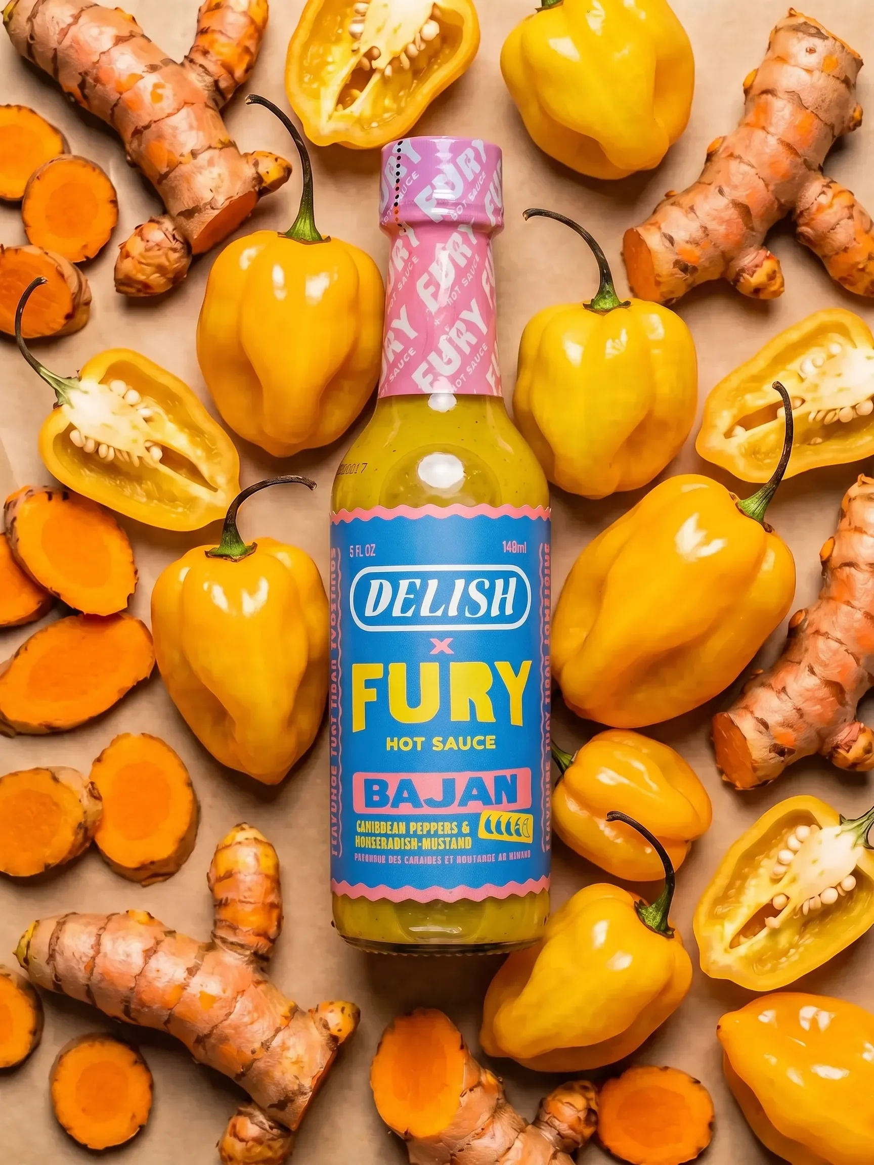 Delish x Fury Bajan hot sauce bottle surrounded by fresh habanero peppers and sliced turmeric root

