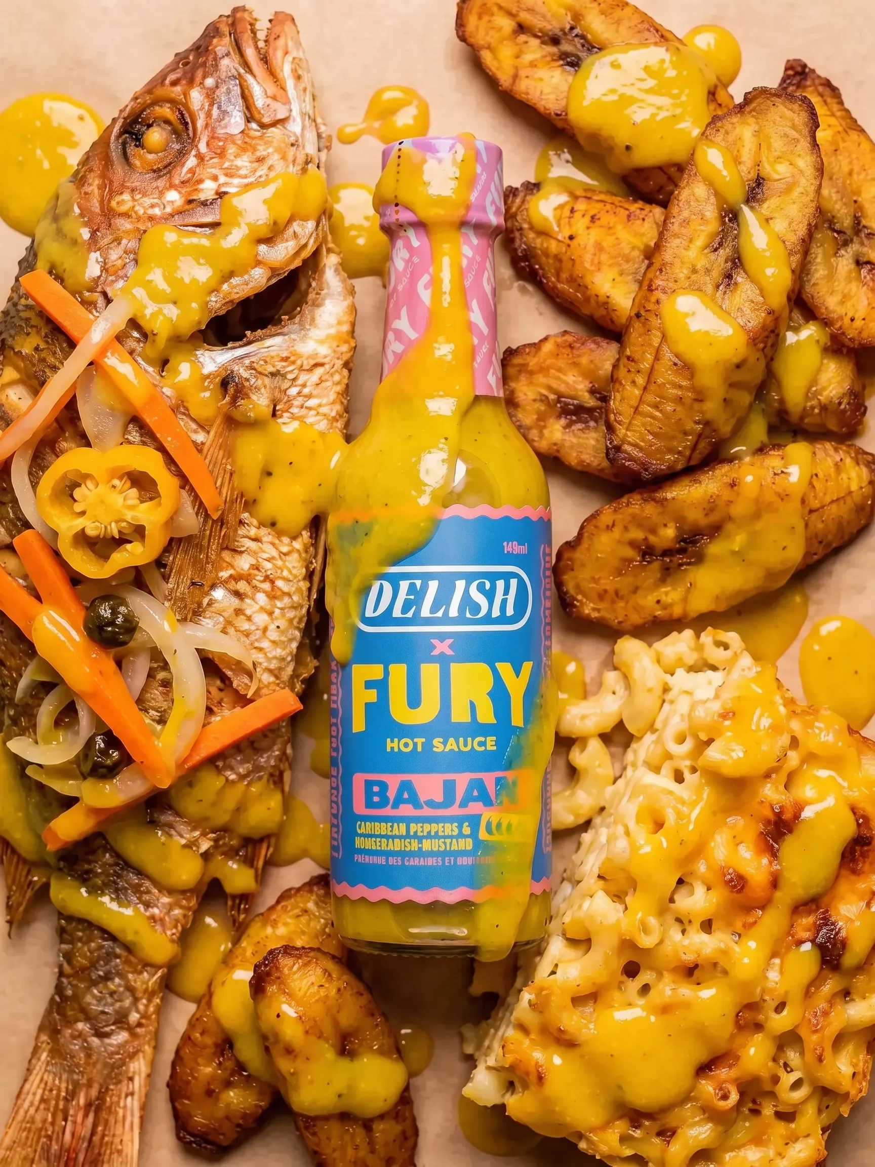 Delish x Fury Bajan hot sauce drizzled over whole fried fish, fried plantains, and mac and cheese
